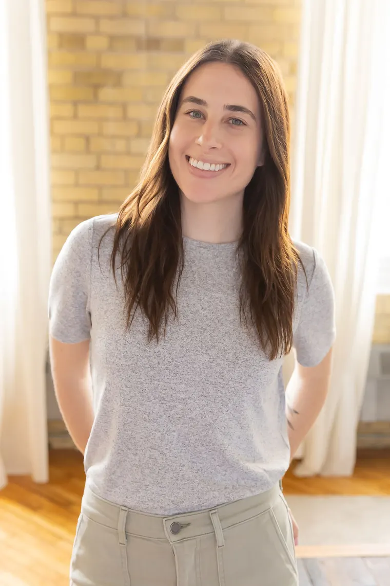 Stephanie Raines smiling, in a grey t-shirt in front of a brick wall